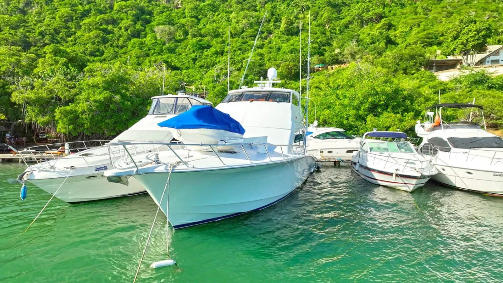 A sleek yacht is docked alongside other boats in a lush, green marina. aboard HATTERAS 68 CONVERTIBLE Yacht for Sale