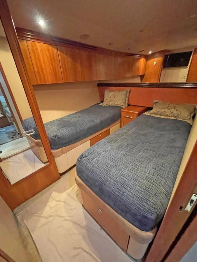 The twin stateroom features two comfortable single beds with elegant bedding and warm wooden finishes. aboard HATTERAS 68 CONVERTIBLE Yacht for Sale