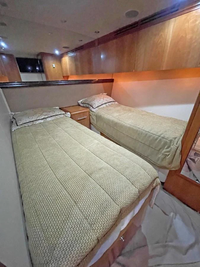 The twin stateroom features two comfortable single beds with elegant bedding and warm wood finishes. aboard HATTERAS 68 CONVERTIBLE Yacht for Sale