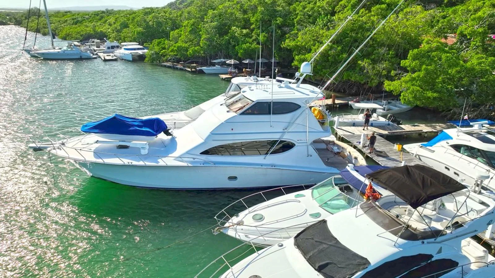 A sleek white yacht is docked in a serene marina surrounded by lush greenery. aboard HATTERAS 68 CONVERTIBLE Yacht for Sale
