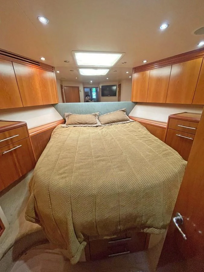The cozy stateroom features a comfortable bed with ample storage and warm wood finishes. aboard HATTERAS 68 CONVERTIBLE Yacht for Sale