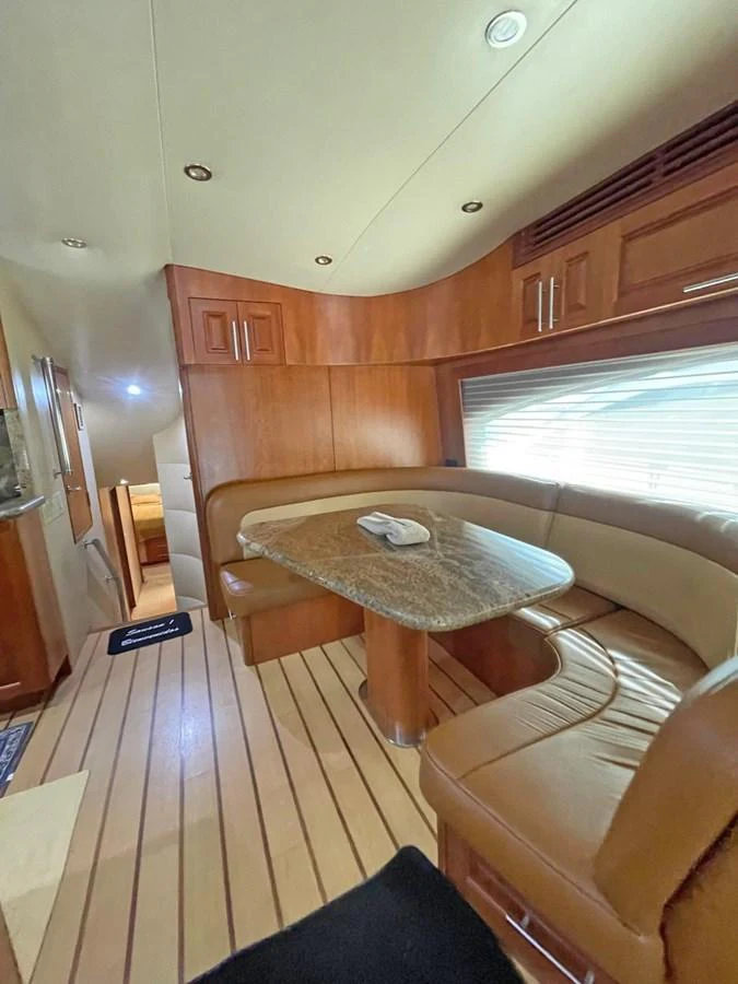 The yacht's interior features a cozy dining area with a curved seating arrangement and a polished table. aboard HATTERAS 68 CONVERTIBLE Yacht for Sale