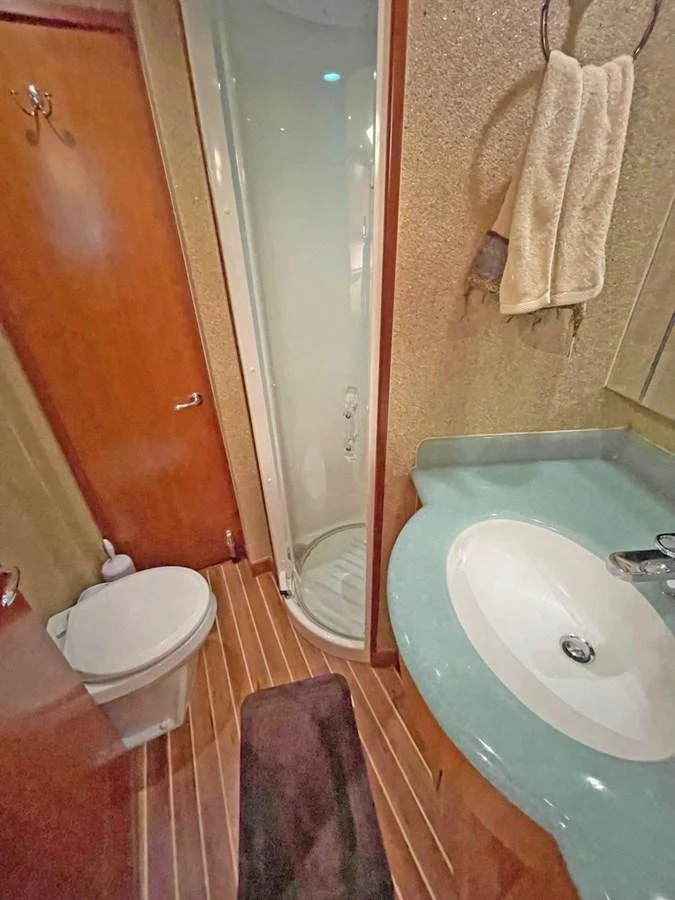A compact yacht bathroom featuring a shower, sink, and toilet with modern fixtures. aboard HATTERAS 68 CONVERTIBLE Yacht for Sale