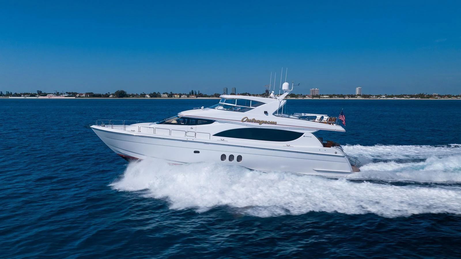 A sleek yacht cruises swiftly on the open water under a clear blue sky. aboard OUTRAGEOUS Yacht for Sale