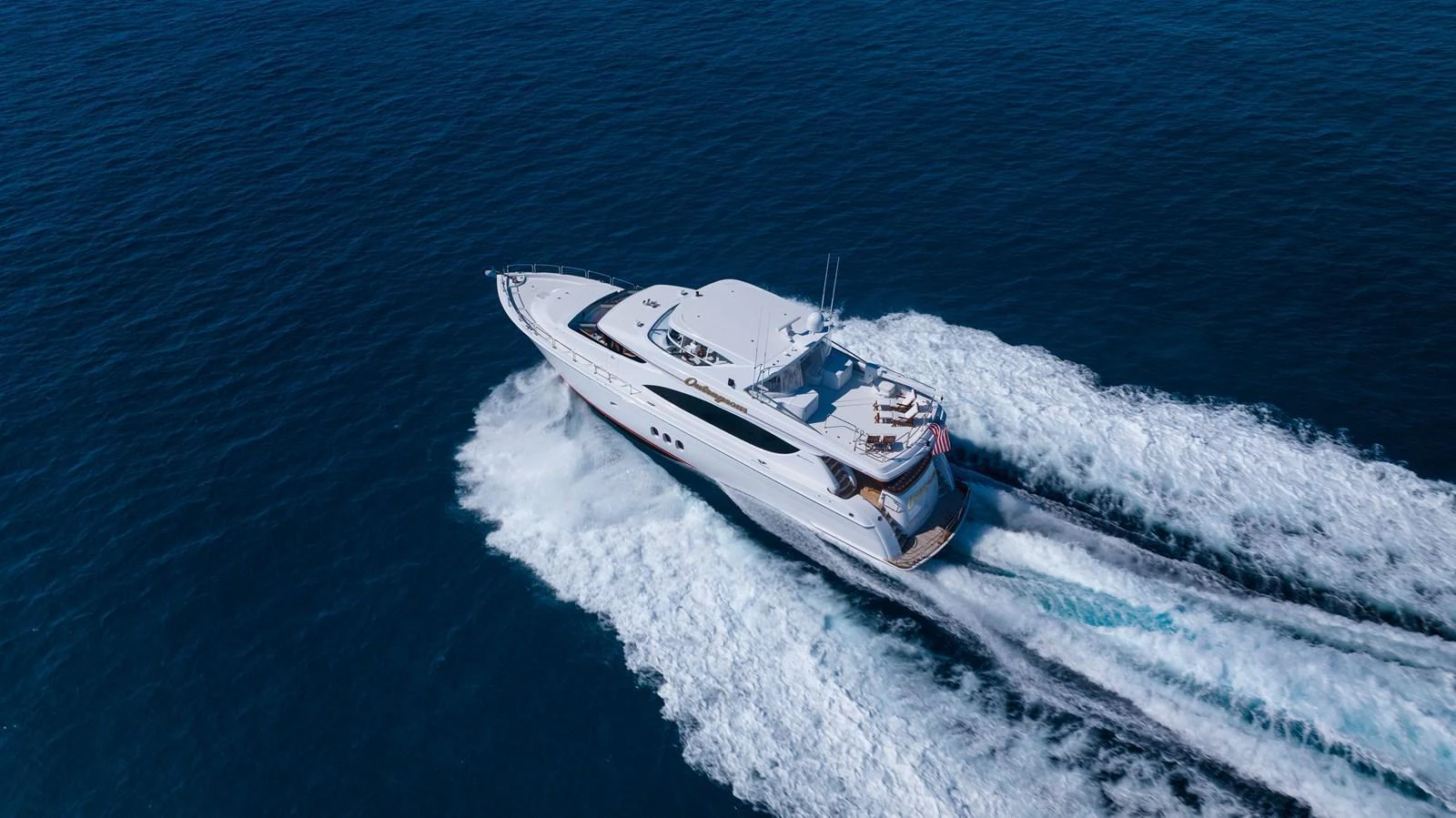 A sleek yacht cruising swiftly on open water, leaving a trail of white wake behind. aboard OUTRAGEOUS Yacht for Sale