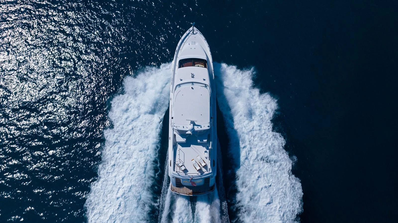 An aerial view of a sleek yacht cruising through the water, leaving a trail of white foam behind. aboard OUTRAGEOUS Yacht for Sale