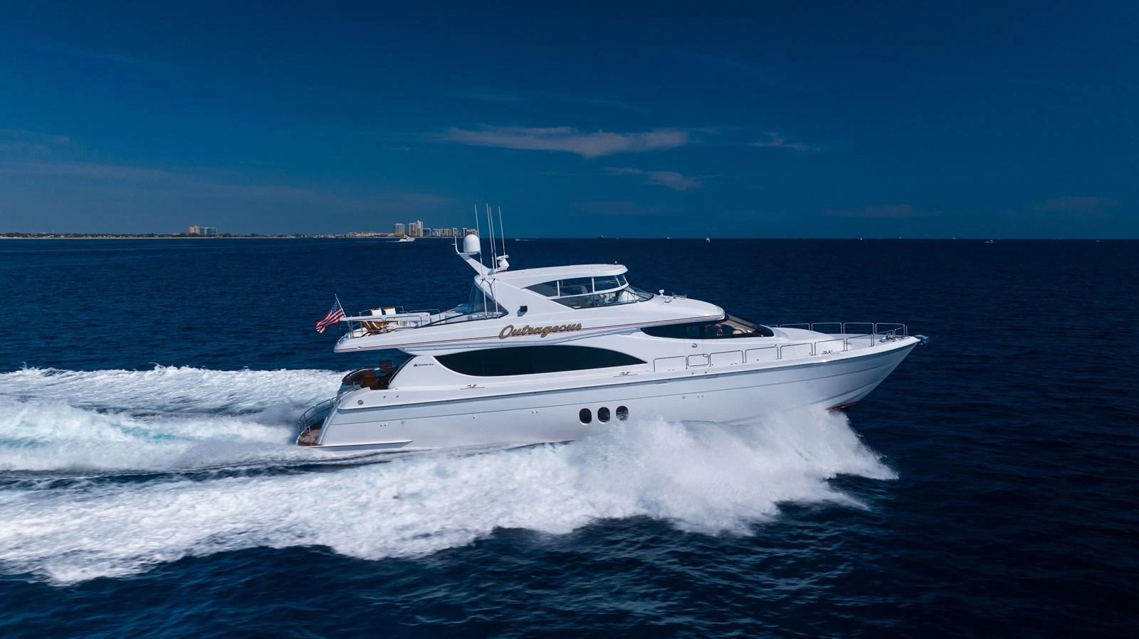 A sleek yacht cruises swiftly through the open water under a clear blue sky. aboard OUTRAGEOUS Yacht for Sale