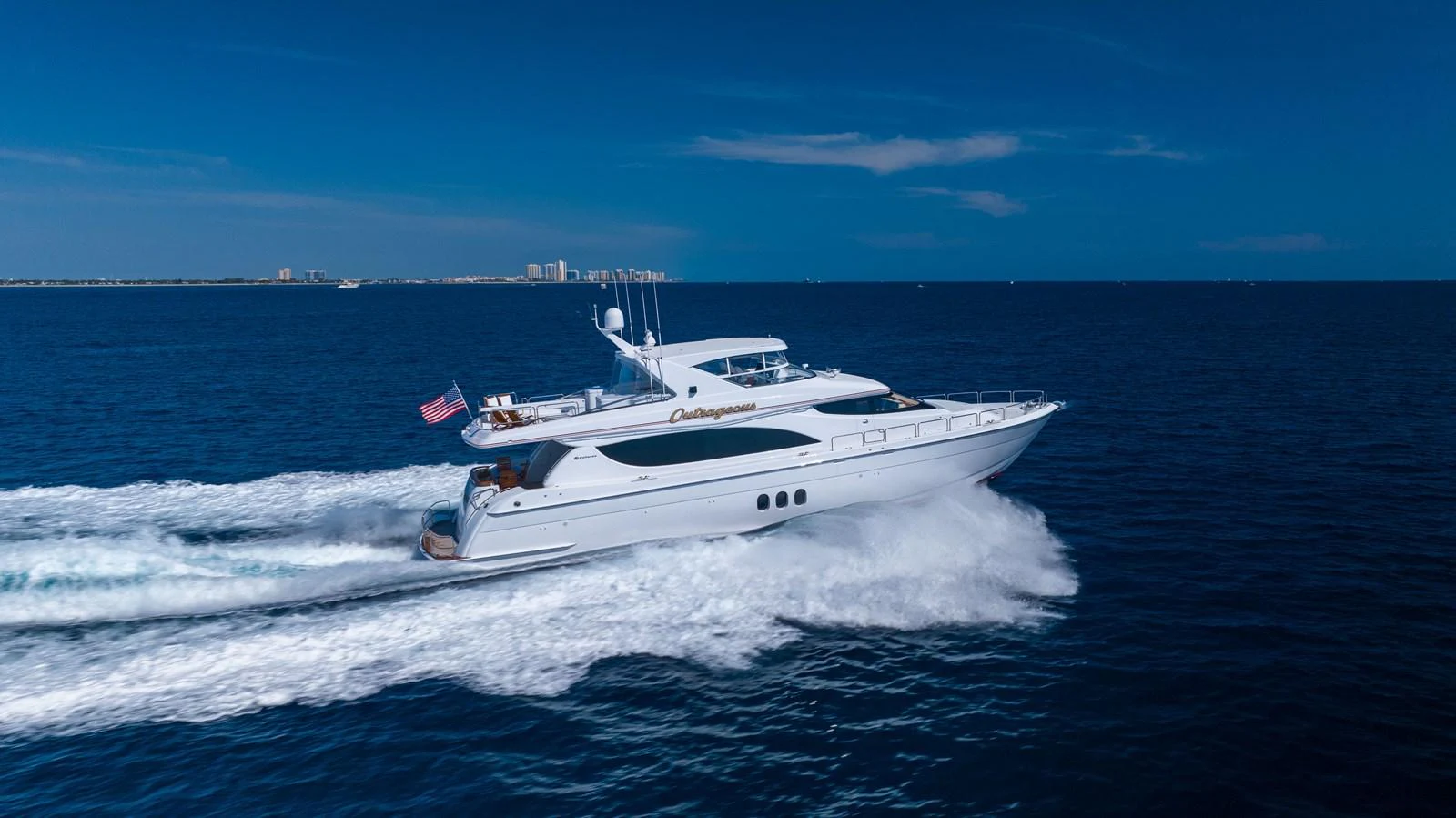 A sleek yacht cruises swiftly across the open sea under a clear blue sky. aboard OUTRAGEOUS Yacht for Sale