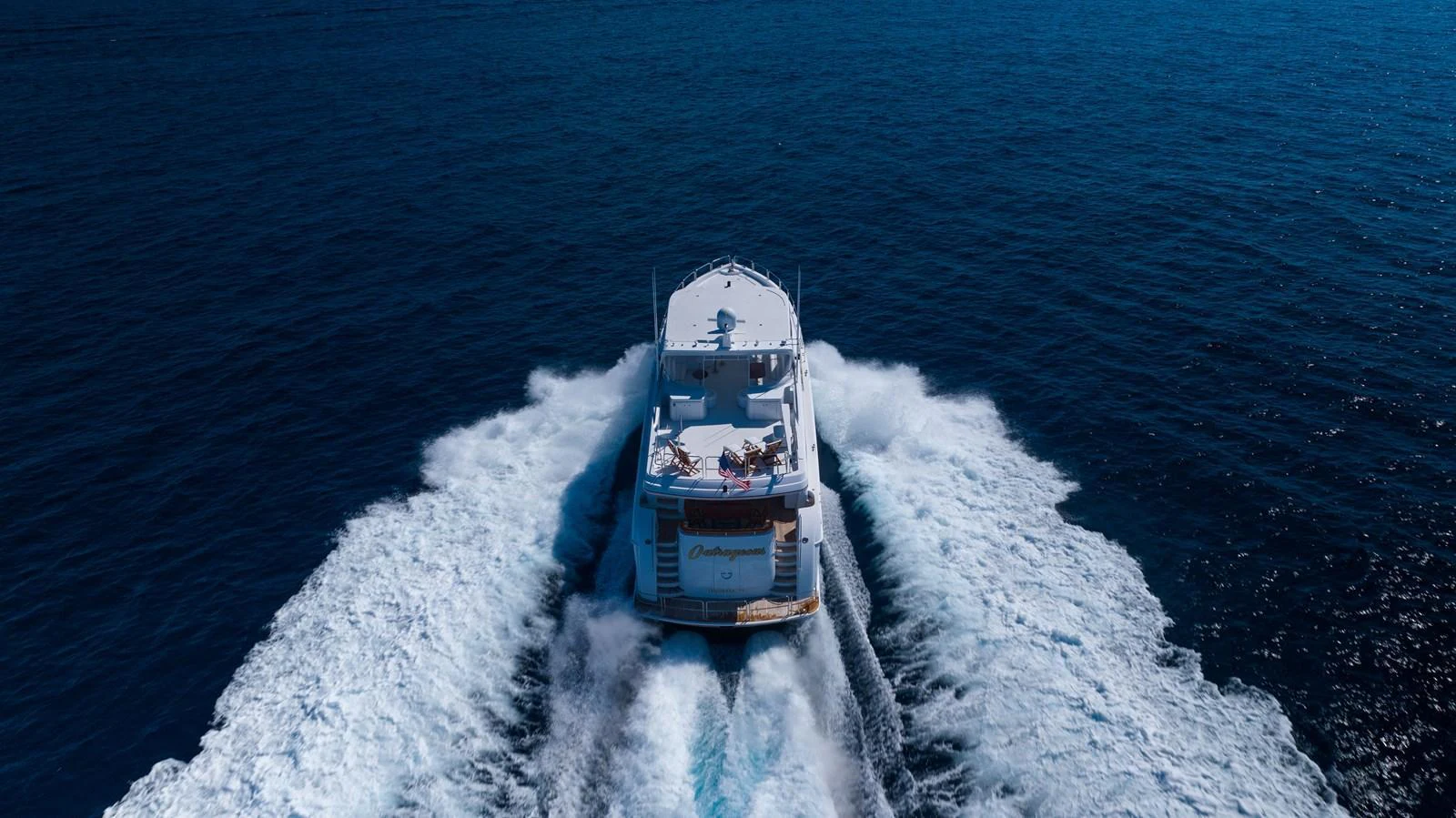 A yacht cruises through the open sea, leaving a trail of white wake behind. aboard OUTRAGEOUS Yacht for Sale
