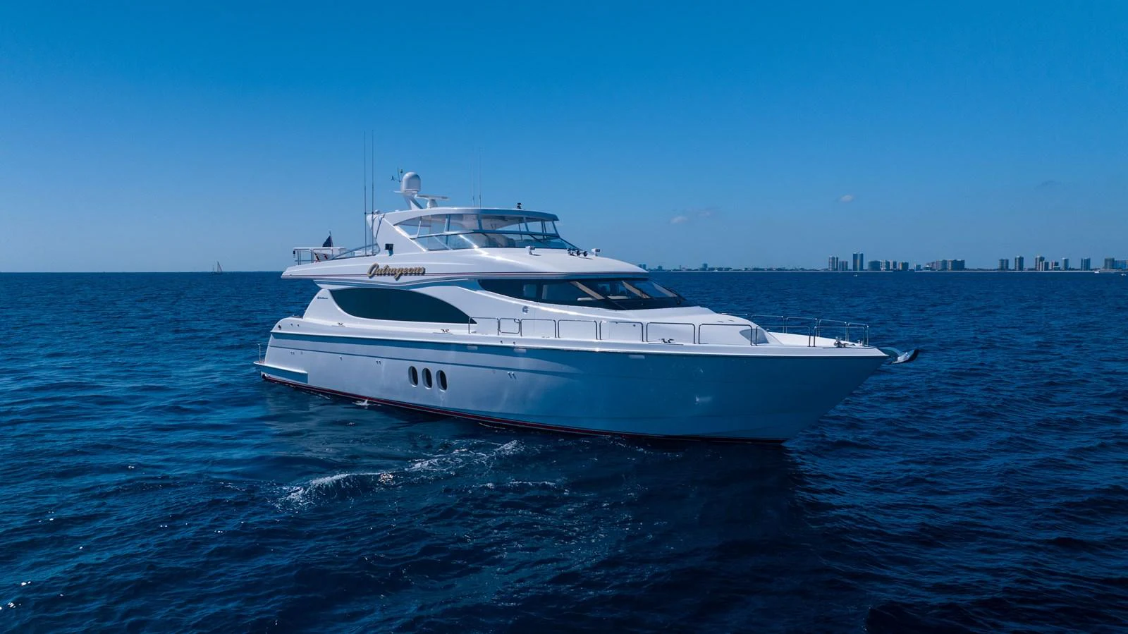 A sleek yacht glides gracefully on the open sea under a clear blue sky. aboard OUTRAGEOUS Yacht for Sale