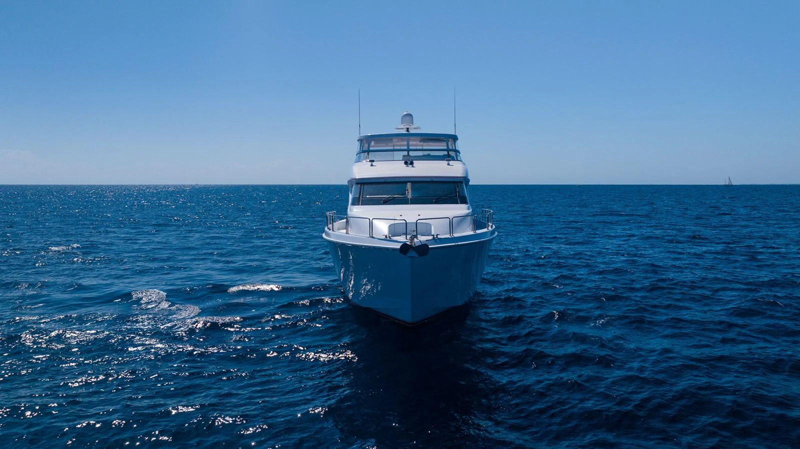 A sleek yacht cruises forward on a calm, open sea under a clear blue sky. aboard OUTRAGEOUS Yacht for Sale