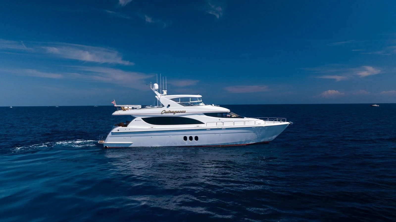 A sleek and elegant yacht cruises smoothly on the open sea under a clear blue sky. aboard OUTRAGEOUS Yacht for Sale