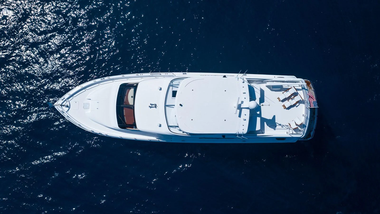Aerial view of a sleek yacht cruising on deep blue waters, showcasing its spacious deck and elegant design. aboard OUTRAGEOUS Yacht for Sale