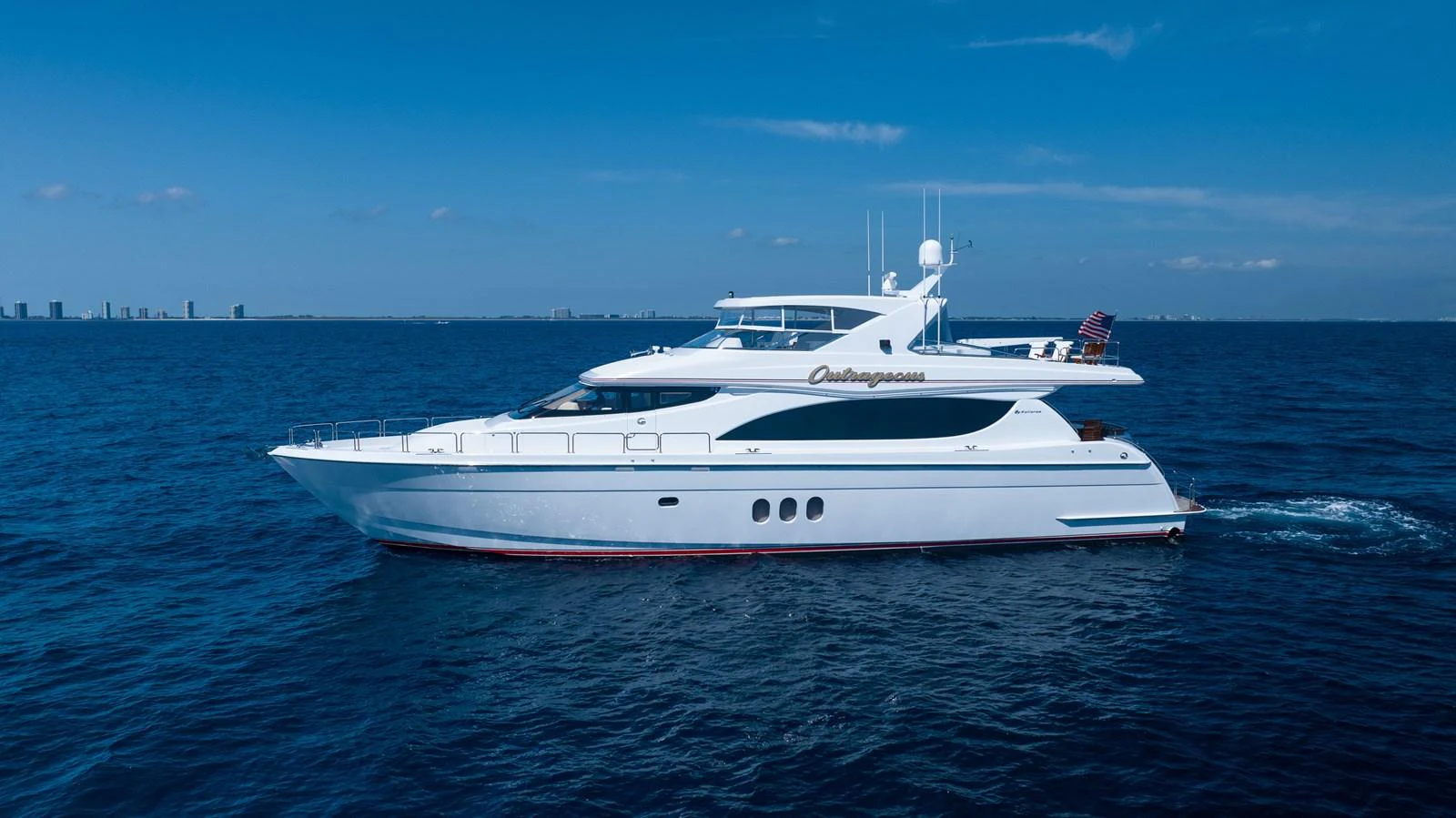 A sleek and modern yacht cruising on calm blue waters under a clear sky. aboard OUTRAGEOUS Yacht for Sale