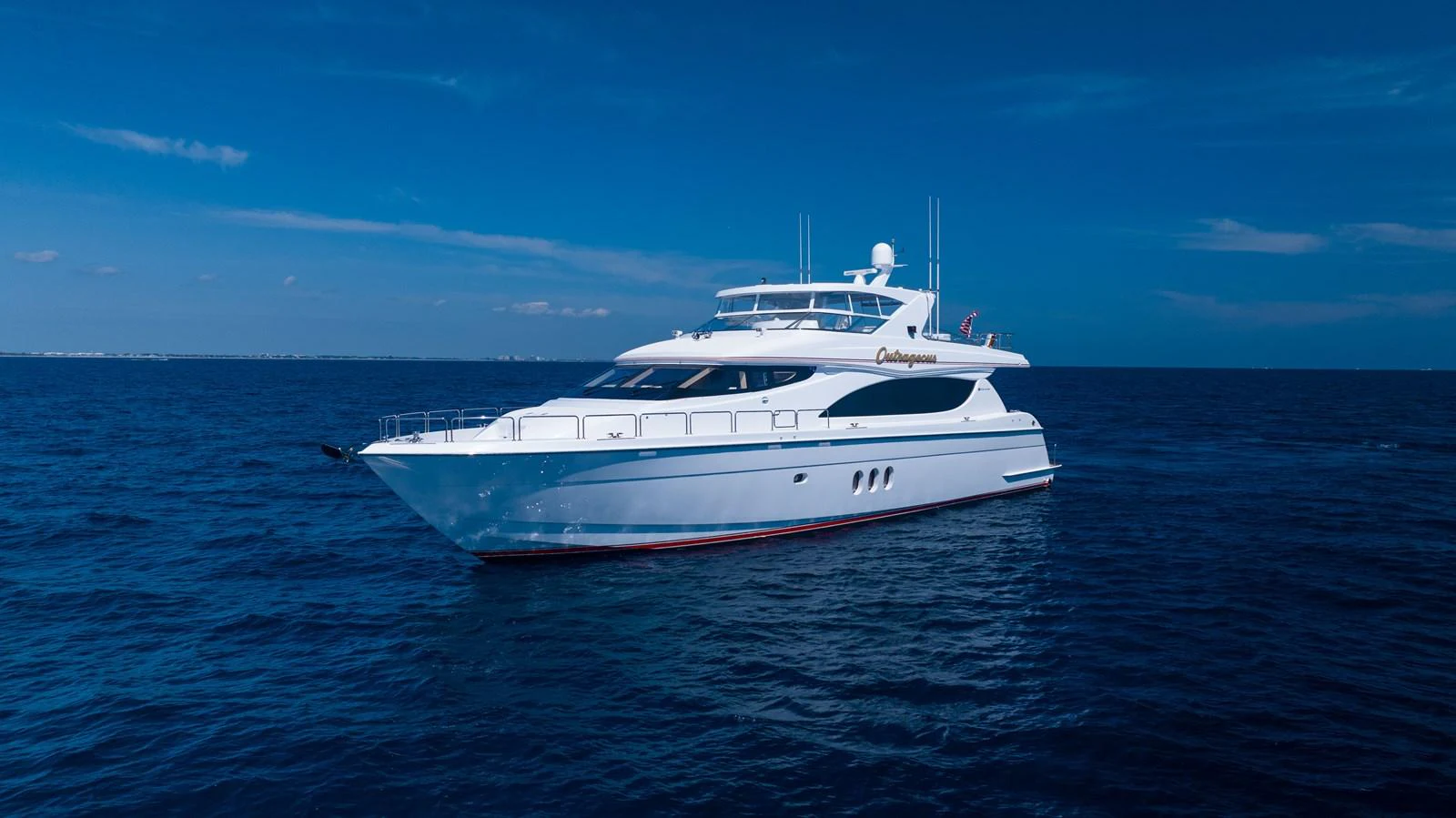 A sleek and modern yacht glides gracefully on the open sea under a clear blue sky. aboard OUTRAGEOUS Yacht for Sale