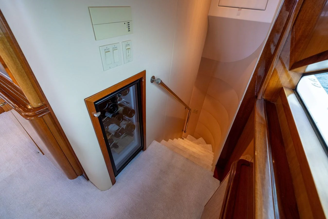 A well-lit staircase with a wine cooler built into the wall, leading to a lower deck. aboard OUTRAGEOUS Yacht for Sale