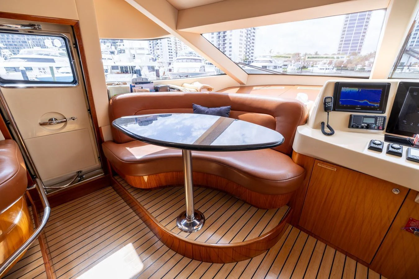 The yacht's saloon features a cozy seating area with a sleek table, complemented by large windows offering a view of the marina. aboard OUTRAGEOUS Yacht for Sale