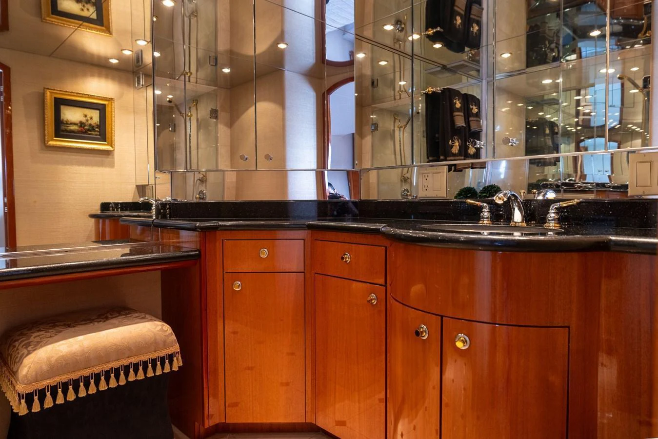 The yacht's bathroom features elegant wooden cabinetry and a sleek black countertop, complemented by mirrored walls. aboard OUTRAGEOUS Yacht for Sale