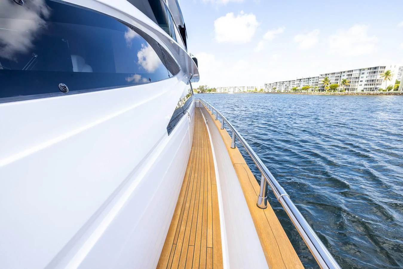 The image captures the sleek side deck of a yacht with a view of the water and distant buildings. aboard SEA METRI V Yacht for Sale