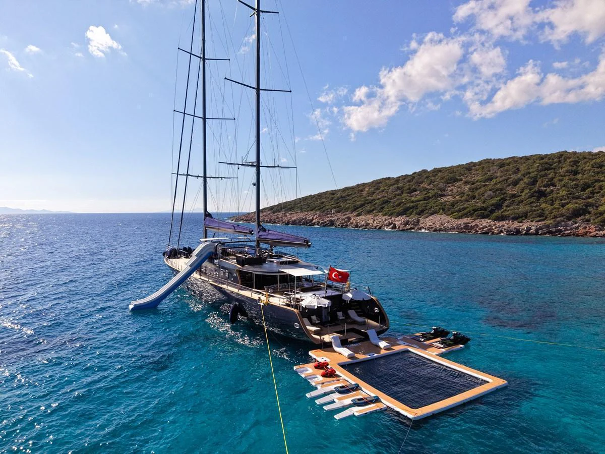 A luxurious yacht anchored in clear blue waters, featuring a slide and a spacious swim platform. aboard OGUZ KHAN Yacht for Sale