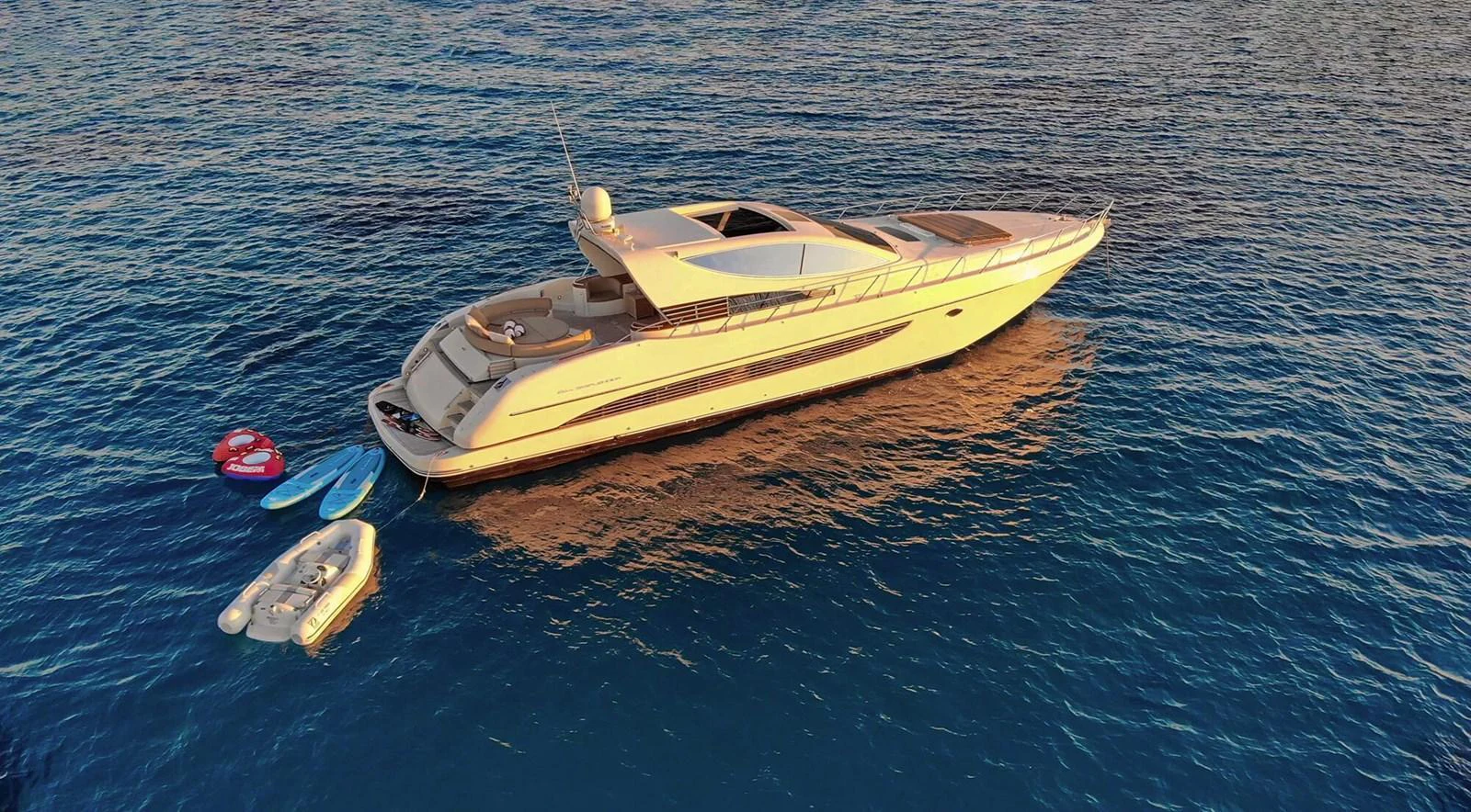 A sleek yacht is anchored on calm waters, with several water toys and a tender floating nearby. aboard RIVA 72' Yacht for Sale