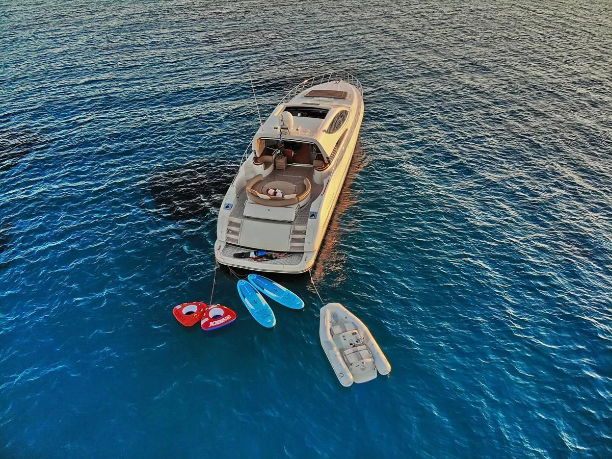 A luxurious yacht is anchored in serene blue waters, accompanied by a tender and several water toys. aboard RIVA 72' Yacht for Sale