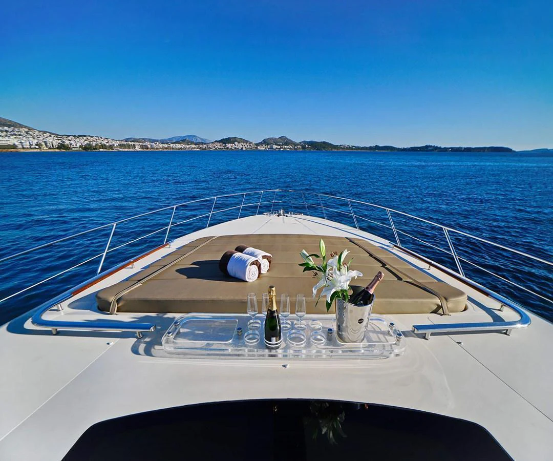 The foredeck of the yacht features a sunpad with towels and a tray with champagne and flowers, set against a stunning ocean backdrop. aboard RIVA 72' Yacht for Sale
