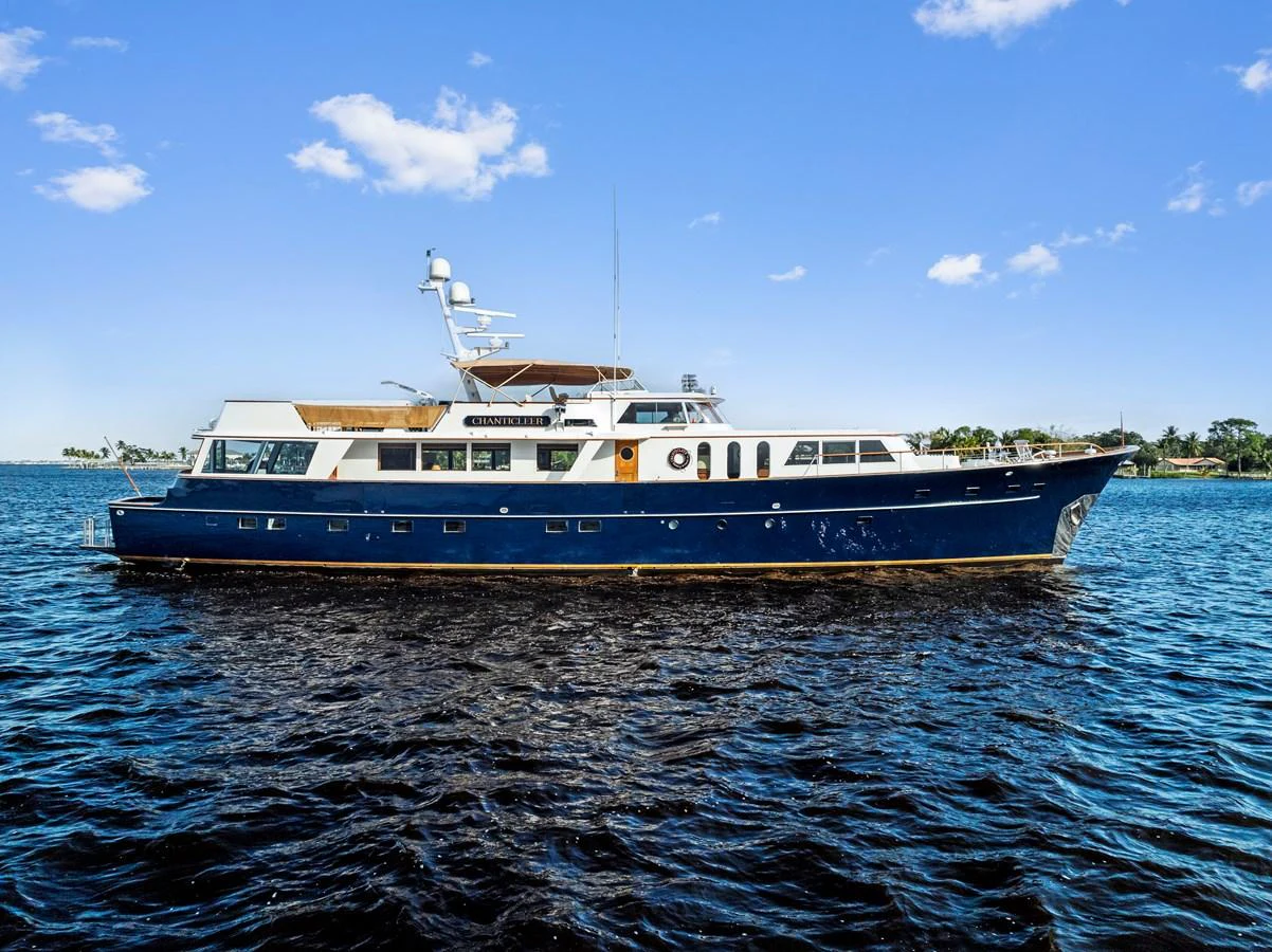 A classic yacht with a sleek blue hull and white superstructure cruising on calm waters under a clear blue sky. aboard CHANTICLEER Yacht for Sale