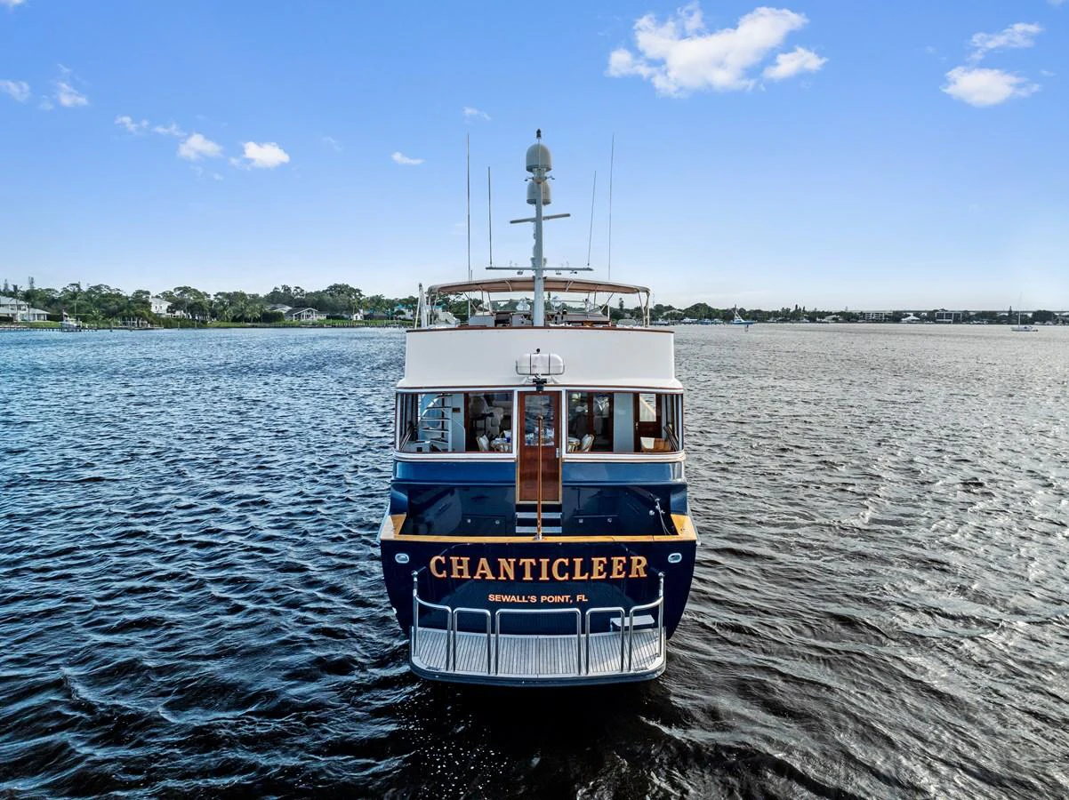 A classic yacht is seen from the rear, cruising on calm waters under a clear blue sky. aboard CHANTICLEER Yacht for Sale