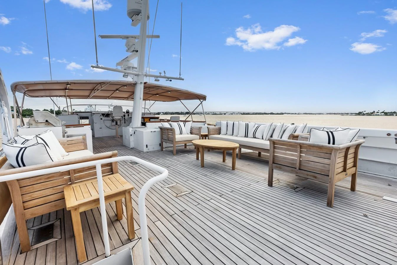 The spacious aft deck features elegant wooden furniture and comfortable seating under a clear blue sky. aboard CHANTICLEER Yacht for Sale
