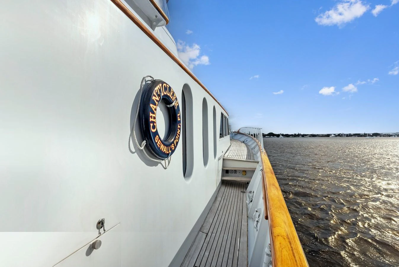 The yacht's exterior showcases a sleek side deck with a view of the water and distant shoreline. aboard CHANTICLEER Yacht for Sale