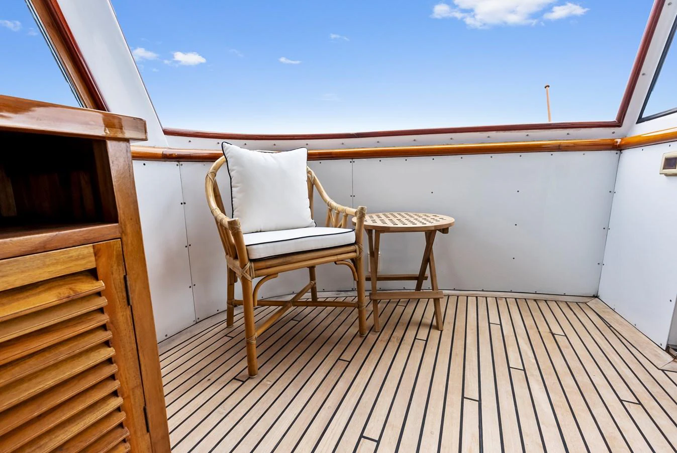 A cozy deck seating area with a wooden chair and table under a clear blue sky. aboard CHANTICLEER Yacht for Sale