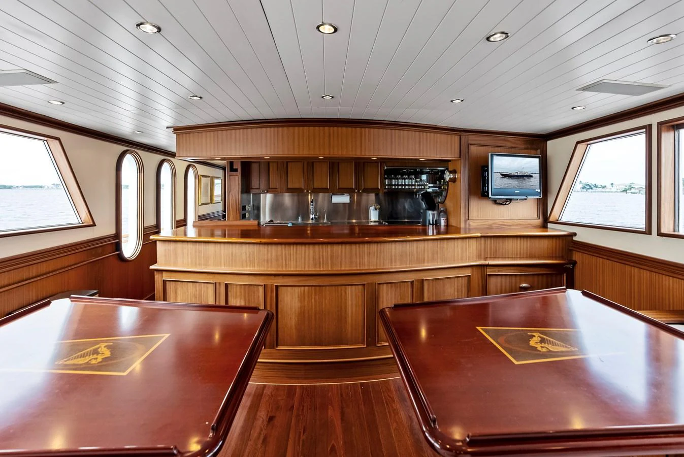 The yacht's interior features a beautifully crafted wooden bar area with ample seating and large windows offering scenic views. aboard CHANTICLEER Yacht for Sale