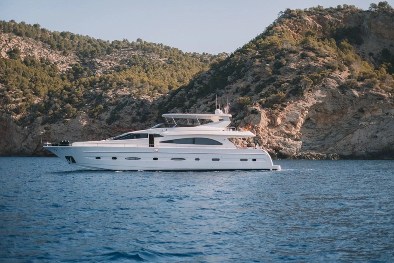 A sleek white yacht cruises along a scenic coastline with lush hills in the background. aboard ASTONDOA 82 GLX Yacht for Sale