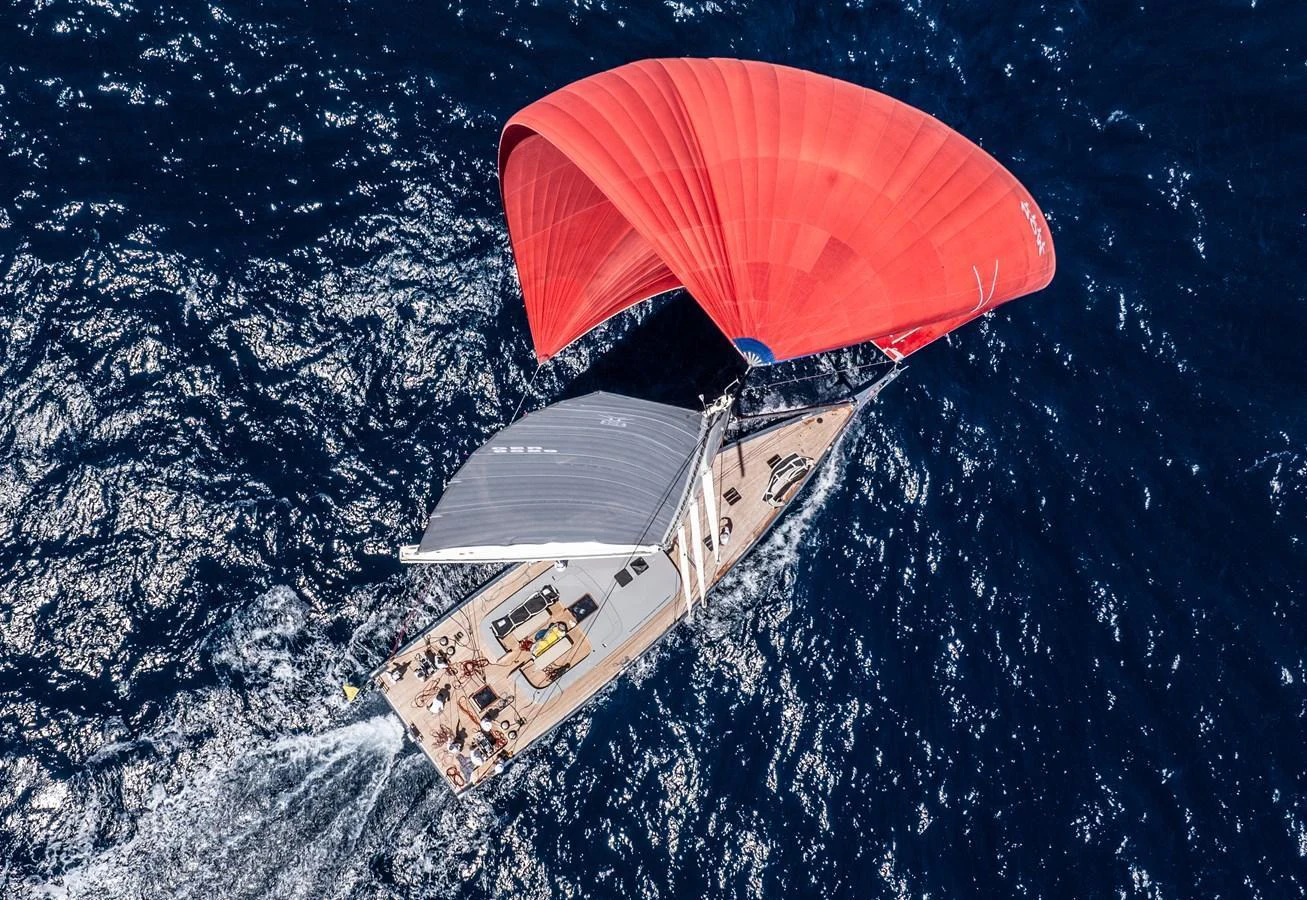 A stunning aerial view of a sailing yacht with vibrant red and white sails cutting through the deep blue ocean. aboard 2026 YYACHTS Y8 Yacht for Sale