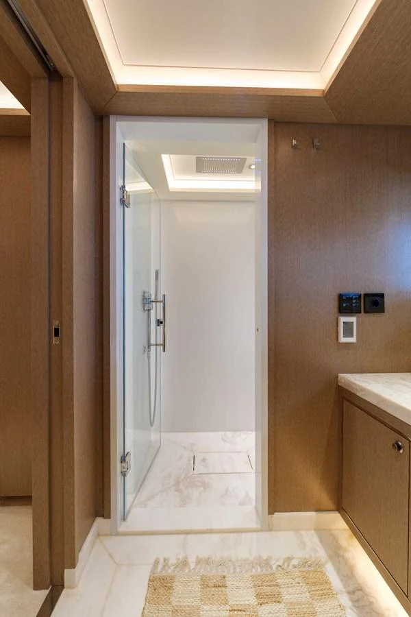 The image showcases a modern yacht bathroom with a glass-enclosed shower and elegant wood paneling. aboard 2024 SIRENA 88 Yacht for Sale