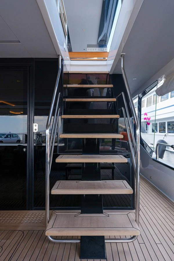 A sleek staircase with wooden steps and stainless steel railings leads to the upper deck. aboard 2024 SIRENA 88 Yacht for Sale