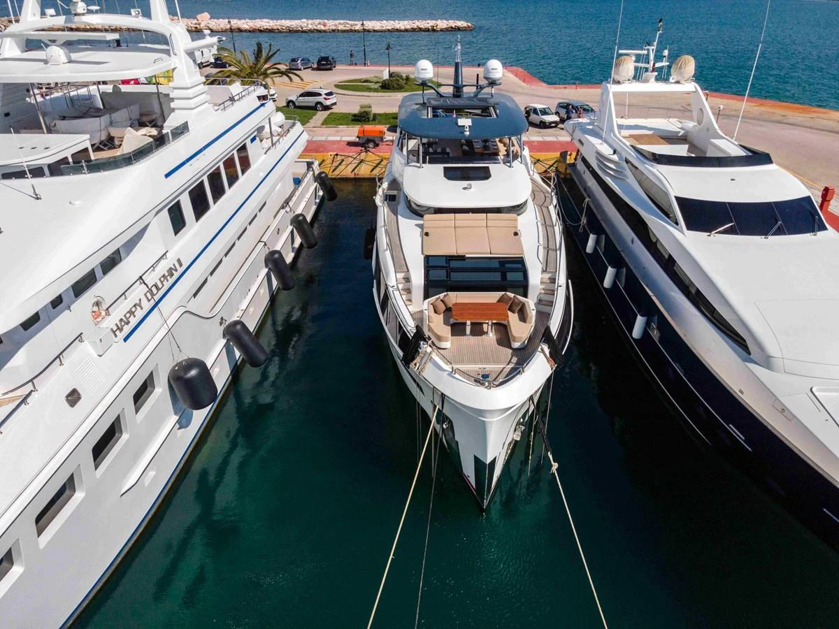 A sleek yacht is docked between two other yachts in a marina, showcasing its modern design and spacious deck. aboard 2024 SIRENA 88 Yacht for Sale
