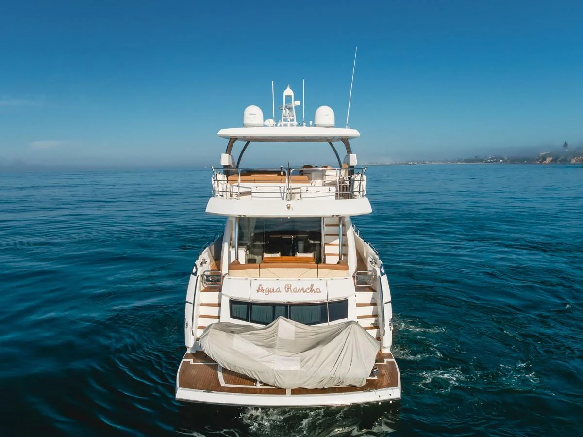 A luxurious yacht is seen from the rear, cruising on calm waters with a clear blue sky above. aboard AGUA RANCHO Yacht for Sale