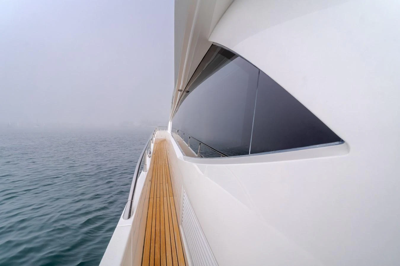 A sleek yacht exterior with a wooden deck and modern design, cruising through a misty seascape. aboard AGUA RANCHO Yacht for Sale