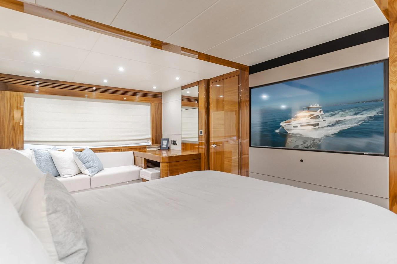The stateroom features a luxurious bed, a cozy seating area, and a large TV displaying a yacht on the water. aboard AGUA RANCHO Yacht for Sale