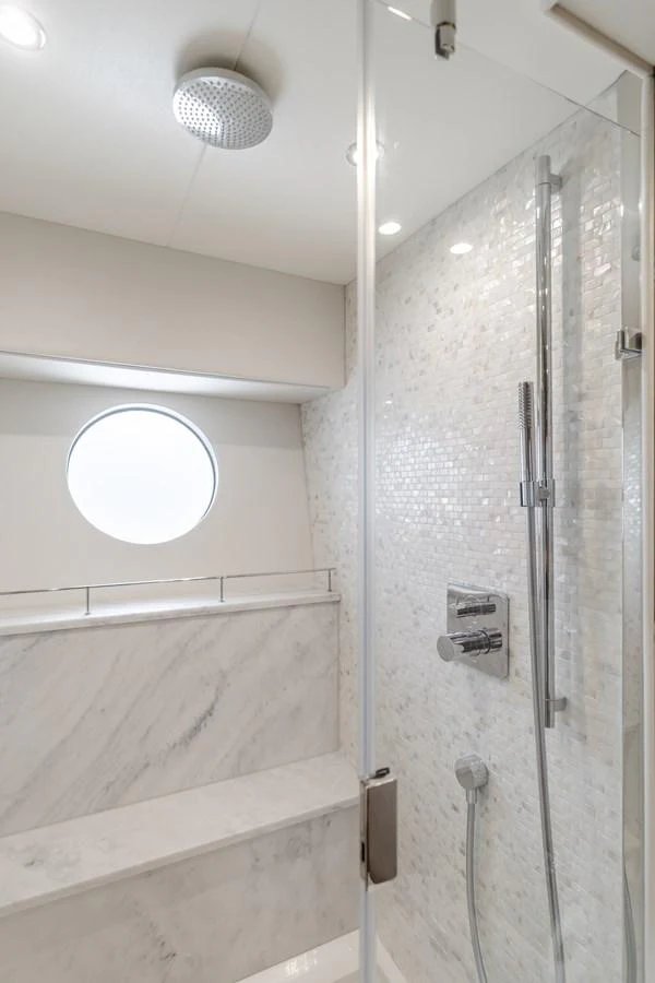 A luxurious yacht bathroom featuring a sleek shower with modern fixtures and a porthole window. aboard AGUA RANCHO Yacht for Sale