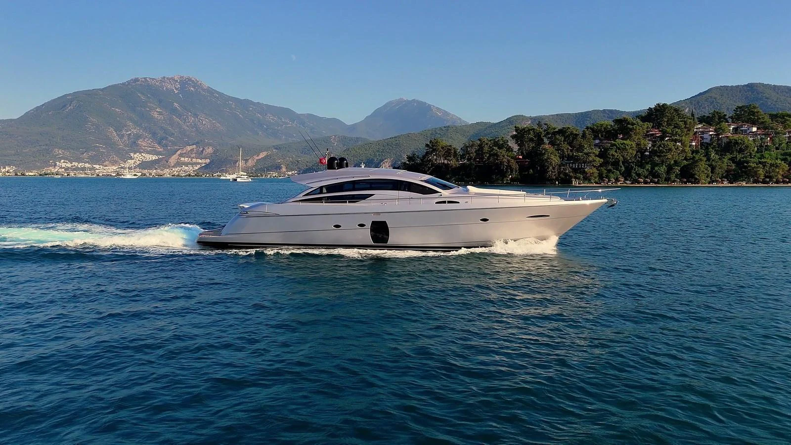 A sleek yacht cruises through calm waters with a scenic mountainous backdrop. aboard FREEDOM 2 Yacht for Sale