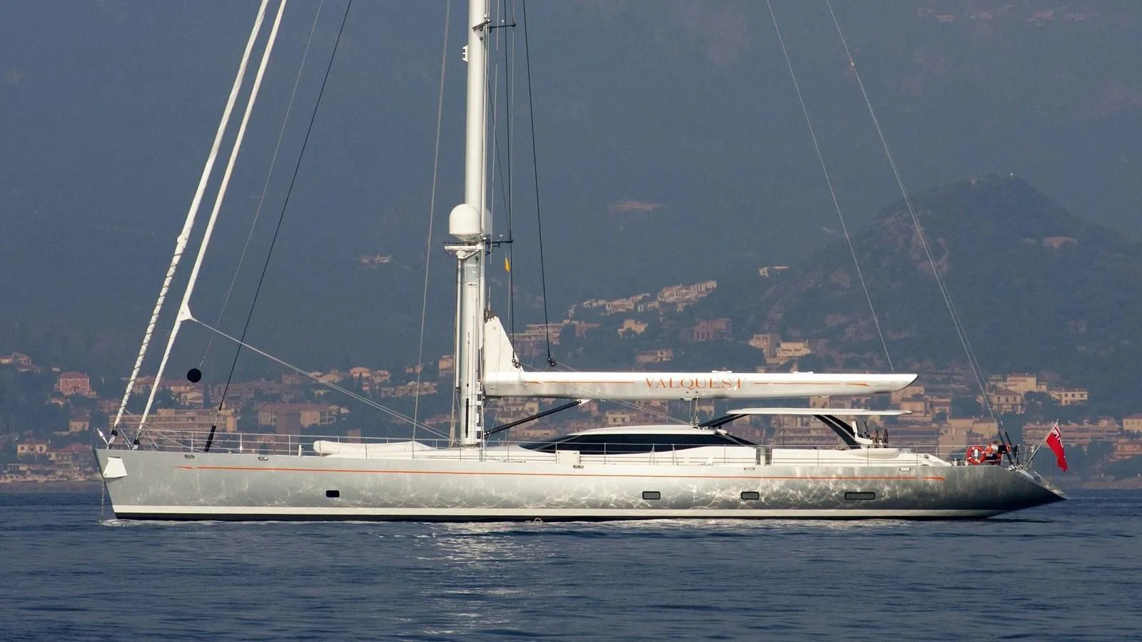 A sleek sailing yacht glides gracefully on calm waters with a scenic mountainous backdrop. aboard VALQUEST Yacht for Sale