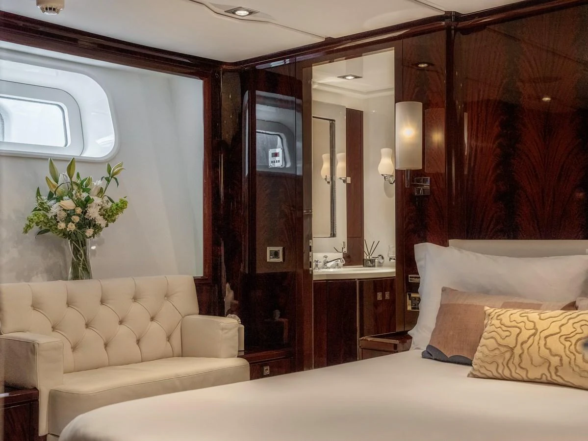 The luxurious stateroom features elegant wood paneling, a plush sofa, and a well-appointed ensuite bathroom. aboard VALQUEST Yacht for Sale