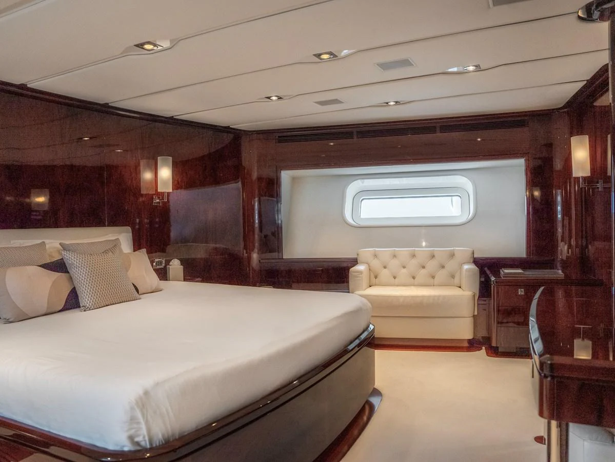 The master stateroom features a luxurious bed, elegant wood paneling, and a comfortable seating area by the window. aboard VALQUEST Yacht for Sale