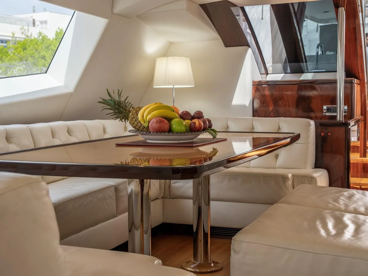 The yacht's salon features a luxurious dining area with a plush, cream-colored seating arrangement and a polished wooden table adorned with fresh fruit. aboard VALQUEST Yacht for Sale