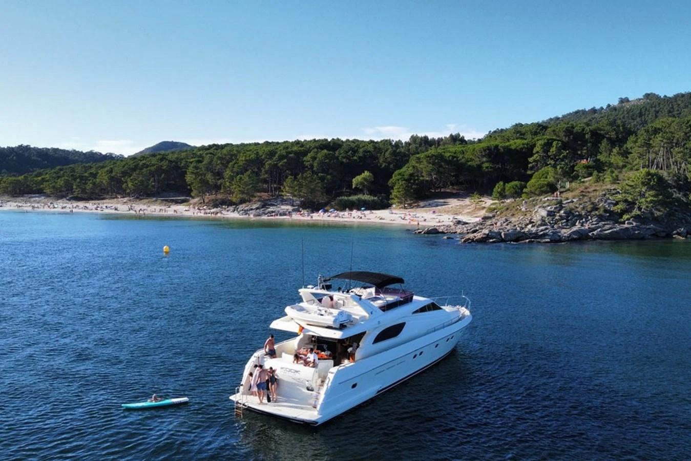 A luxurious yacht is anchored near a scenic coastline with people enjoying the water and sunbathing on the deck. aboard FERRETTI 70 Yacht for Sale