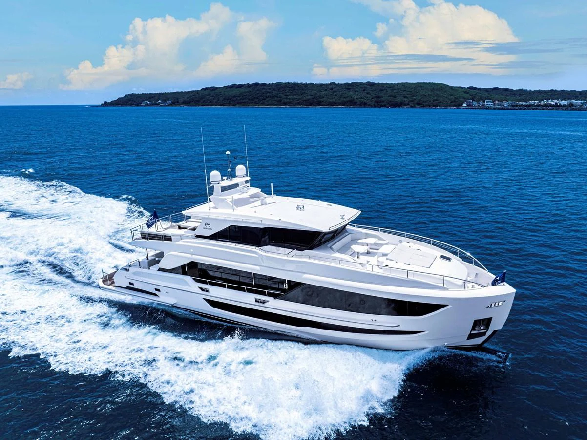 A sleek, modern yacht cruises through the open water against a backdrop of lush coastline and blue skies. aboard HORIZON FD90 Yacht for Sale