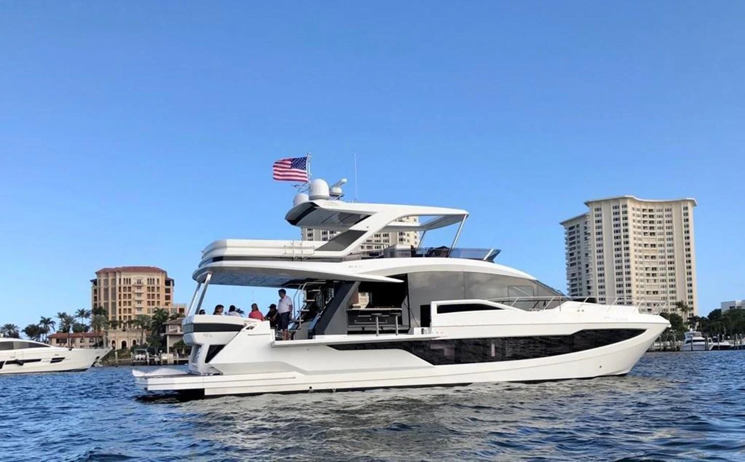 A sleek, modern yacht cruising on the water with a cityscape in the background. aboard GODSPEED Yacht for Sale